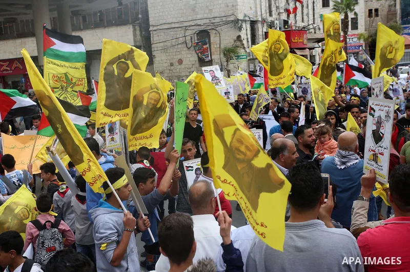 Palestinian protesters wave flags bearing the portrait of prominent prisoner and popular leader Marwan Barghouti during a demonstration in solidarity with Palestinian prisoners on hunger strike in Israeli jails, in the W...
