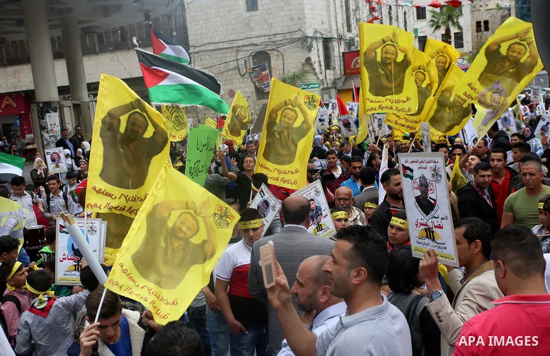 Palestinian protesters wave flags bearing the portrait of prominent prisoner and popular leader Marwan Barghouti during a demonstration in solidarity with Palestinian prisoners on hunger strike in Israeli jails, in the W...