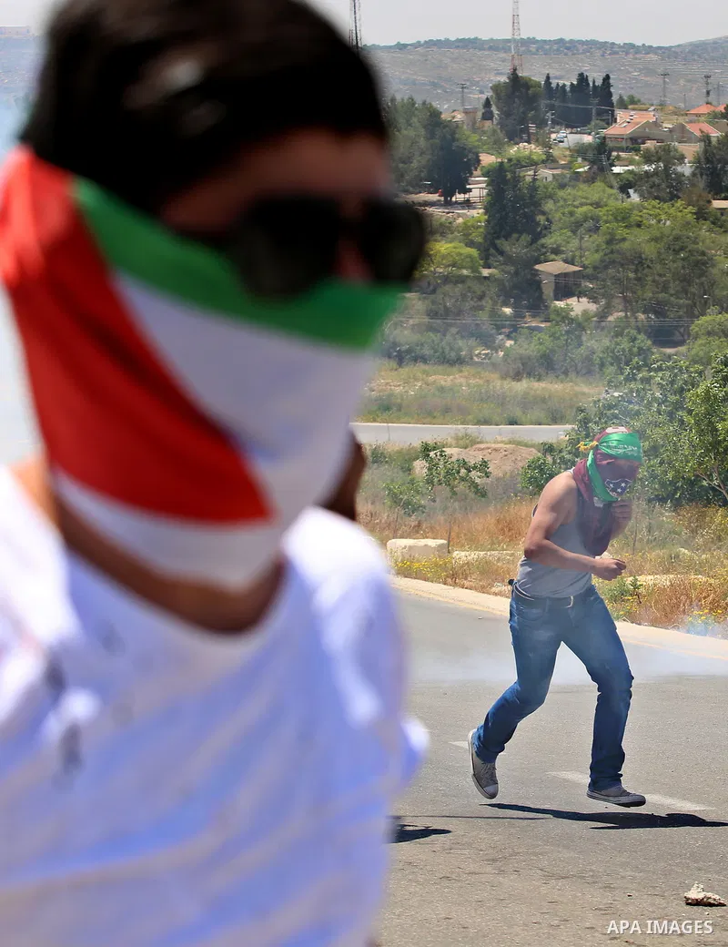 Palestinian protesters run for a cover from a tear gas canister fired by Israeli security forces during clashes at a protest in support of Palestinian prisoners on hunger strike in Israeli jails, in the West Bank village...