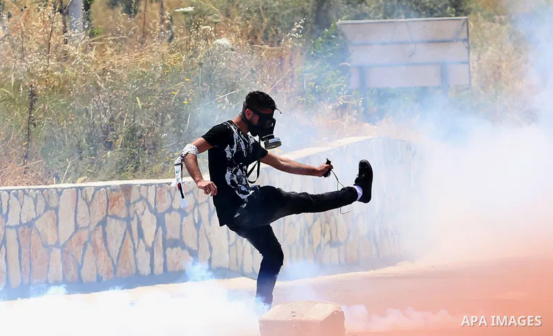 A Palestinian protester kicks back a tear gas canister fired by Israeli security forces during clashes at a protest in support of Palestinian prisoners on hunger strike in Israeli jails, in the West Bank village of al-Na...