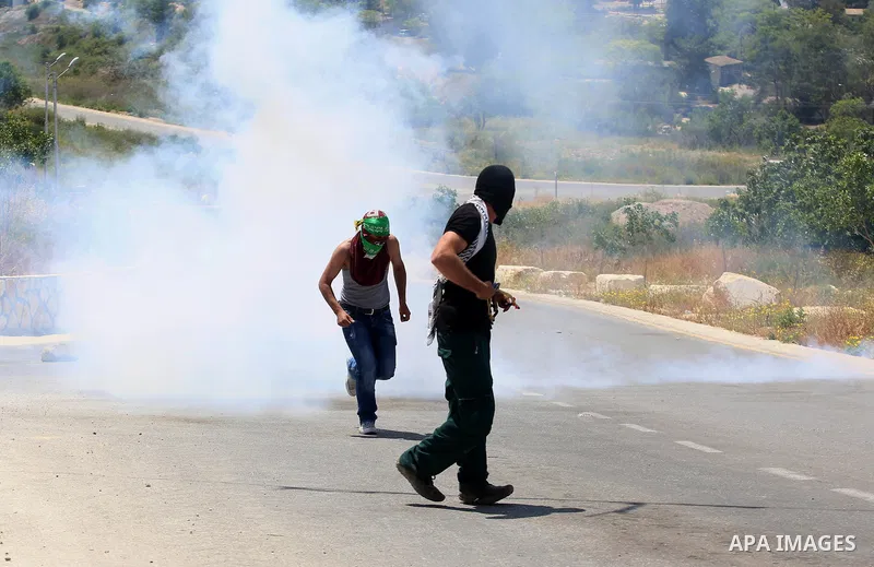 Palestinian protesters run for a cover from a tear gas canister fired by Israeli security forces during clashes at a protest in support of Palestinian prisoners on hunger strike in Israeli jails, in the West Bank village...