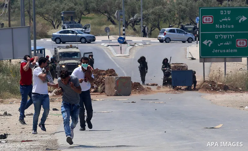 Palestinian protesters run for a cover from a tear gas canister fired by Israeli security forces during clashes at a protest in support of Palestinian prisoners on hunger strike in Israeli jails, in the West Bank village...