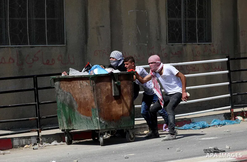 Palestinian protesters take cover from a tear gas canister fired by Israeli security forces during clashes at a protest in support of Palestinian prisoners on hunger strike in Israeli jails, in the West Bank village of B...