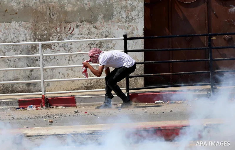 A Palestinian protester takes cover from a tear gas canister fired by Israeli security forces during clashes at a protest in support of Palestinian prisoners on hunger strike in Israeli jails, in the West Bank village of...
