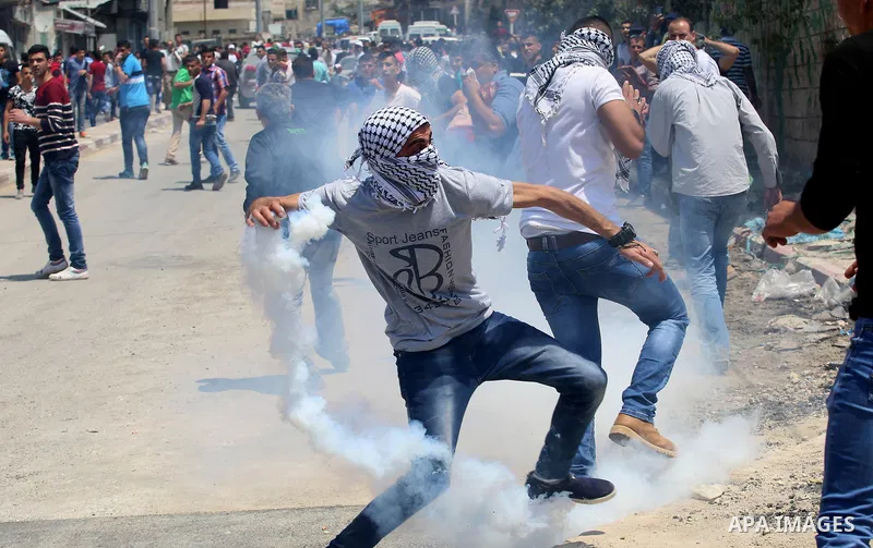 A Palestinian protester throws back a tear gas canister fired by Israeli security forces during clashes at a protest in support of Palestinian prisoners on hunger strike in Israeli jails, in the West Bank village of Beit...