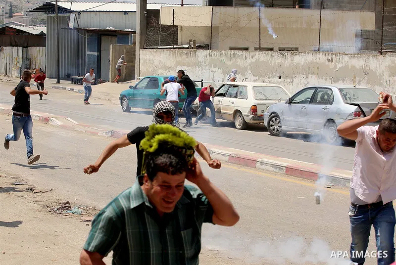 Palestinian protesters run for a cover from a tear gas canister fired by Israeli security forces during clashes at a protest in support of Palestinian prisoners on hunger strike in Israeli jails, in the West Bank village...