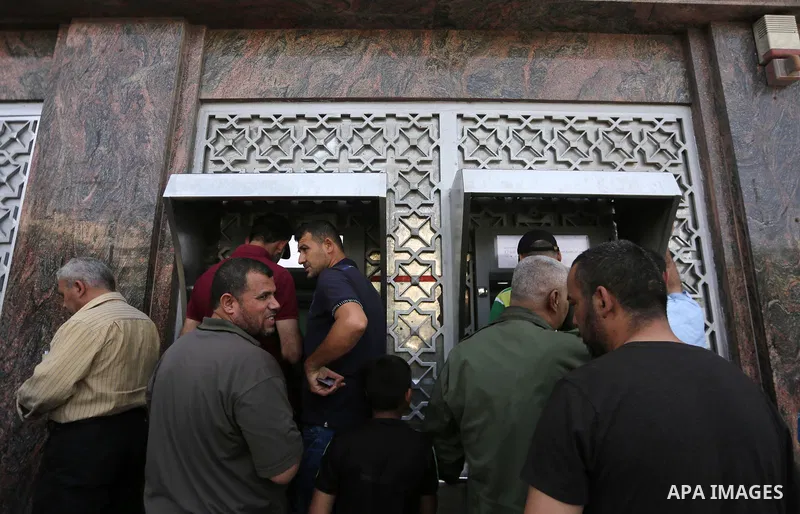 Palestinians, employed by the Palestinian Authority wait to receive their salaries from an ATM, outside a Bank in Gaza City on May 10, 2017. The salaries of Palestinian employees in Gaza strip have been reduced by about...