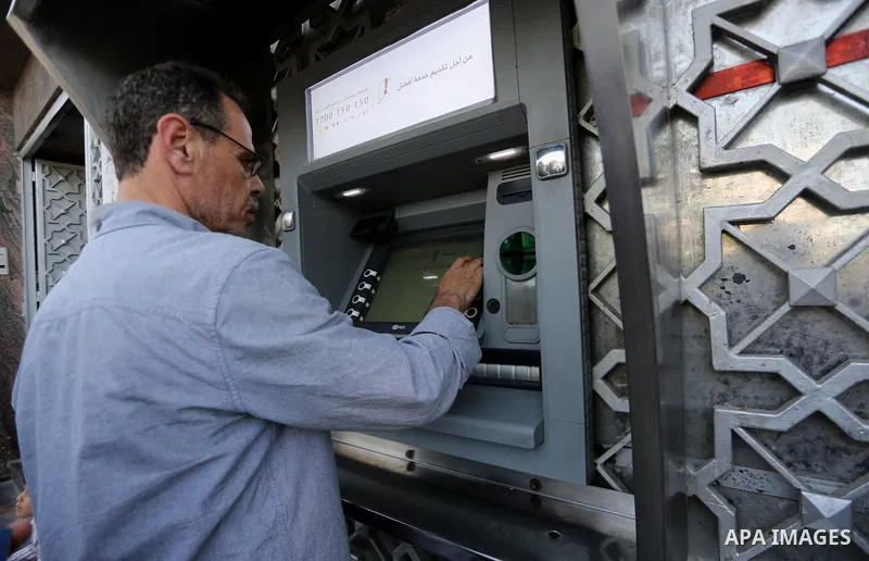 Palestinians, employed by the Palestinian Authority wait to receive their salaries from an ATM, outside a Bank in Gaza City on May 10, 2017. The salaries of Palestinian employees in Gaza strip have been reduced by about...