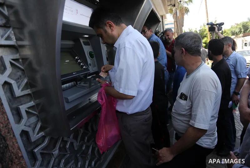 Palestinians, employed by the Palestinian Authority wait to receive their salaries from an ATM, outside a Bank in Gaza City on May 10, 2017. The salaries of Palestinian employees in Gaza strip have been reduced by about...