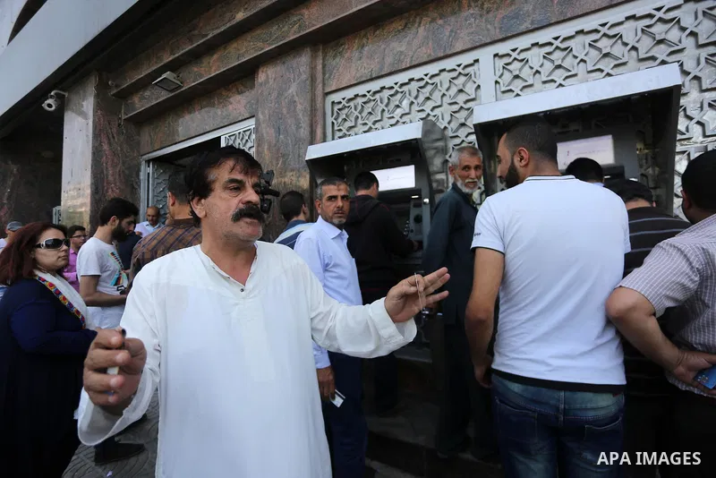 Palestinians, employed by the Palestinian Authority wait to receive their salaries from an ATM, outside a Bank in Gaza City on May 10, 2017. The salaries of Palestinian employees in Gaza strip have been reduced by about...