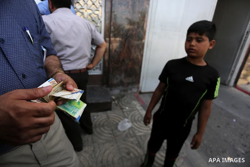 Palestinians, employed by the Palestinian Authority wait to receive their salaries from an ATM, outside a Bank in Gaza City on May 10, 2017. The salaries of Palestinian employees in Gaza strip have been reduced by about...