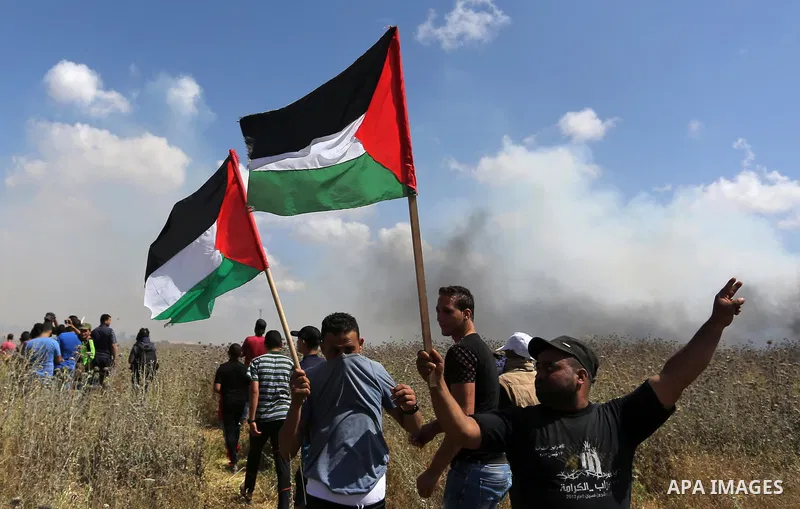 Palestinian protesters wave a national flag during clashes with Israeli security forces following a protest against the blockade on Gaza Strip, near Nahal Oz crossing east of Gaza City on May 19, 2017. Photo by Ashraf Am...