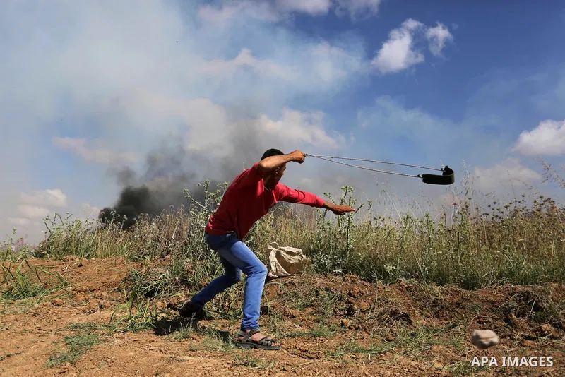 A Palestinian protester uses a slingshot to hurl stones towards Israeli security forces during clashes following a protest against the blockade on Gaza Strip, near Nahal Oz crossing east of Gaza City on May 19, 2017. Pho...