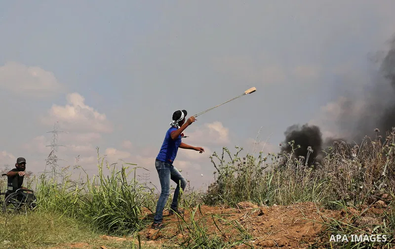 A Palestinian protester uses a slingshot to hurl stones towards Israeli security forces during clashes following a protest against the blockade on Gaza Strip, near Nahal Oz crossing east of Gaza City on May 19, 2017. Pho...