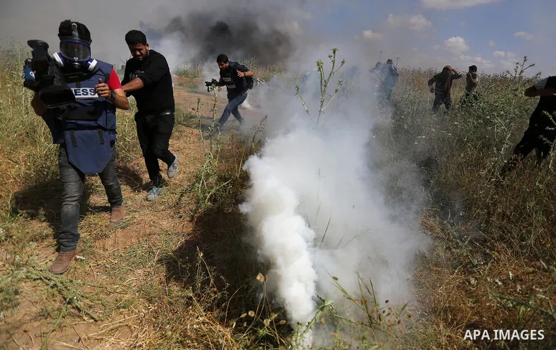 Palestinian photographers take cover from tear gas fired by Israeli security forces during clashes following a protest against the blockade on Gaza Strip, near Nahal Oz crossing east of Gaza City on May 19, 2017. Photo b...