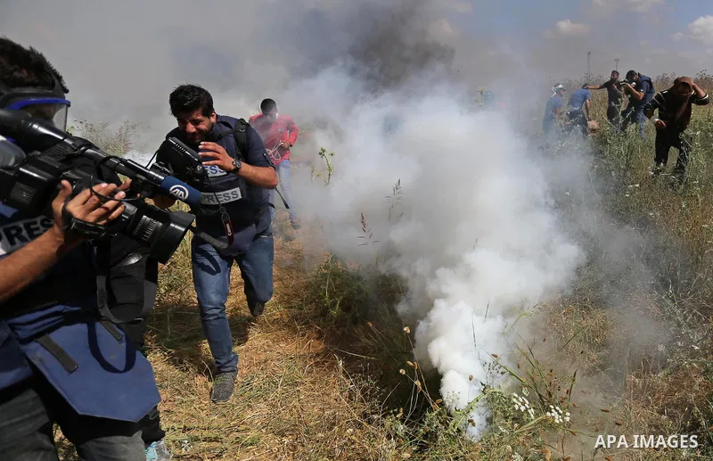 Palestinian photographers take cover from tear gas fired by Israeli security forces during clashes following a protest against the blockade on Gaza Strip, near Nahal Oz crossing east of Gaza City on May 19, 2017. Photo b...