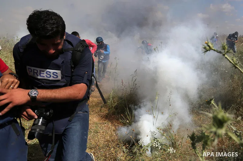 Palestinian photographers take cover from tear gas fired by Israeli security forces during clashes following a protest against the blockade on Gaza Strip, near Nahal Oz crossing east of Gaza City on May 19, 2017. Photo b...