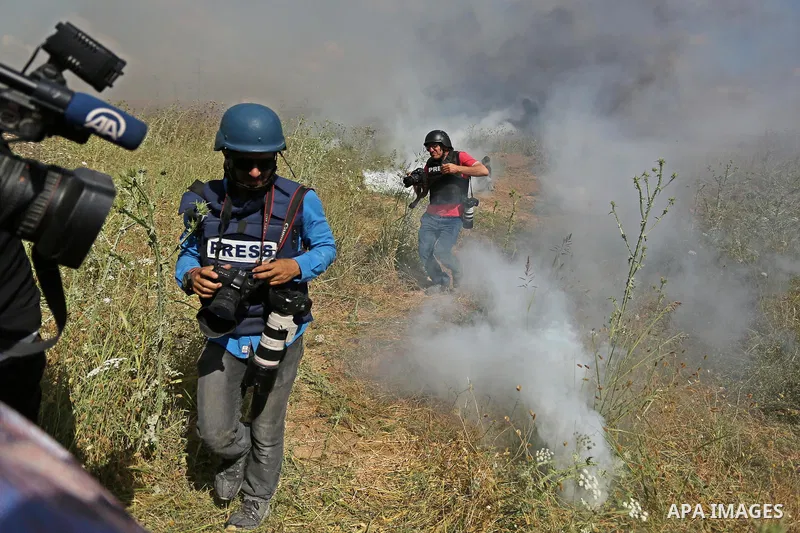 Palestinian photographers take cover from tear gas fired by Israeli security forces during clashes following a protest against the blockade on Gaza Strip, near Nahal Oz crossing east of Gaza City on May 19, 2017. Photo b...