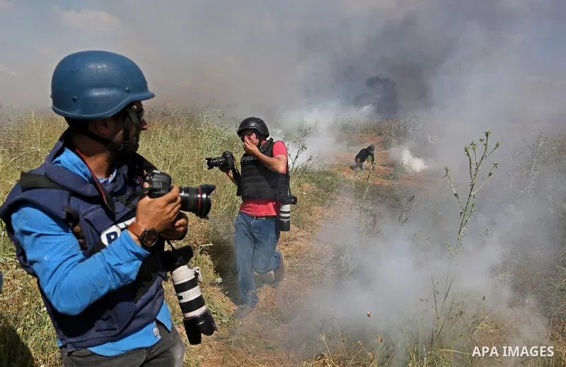 Palestinian photographers take cover from tear gas fired by Israeli security forces during clashes following a protest against the blockade on Gaza Strip, near Nahal Oz crossing east of Gaza City on May 19, 2017. Photo b...