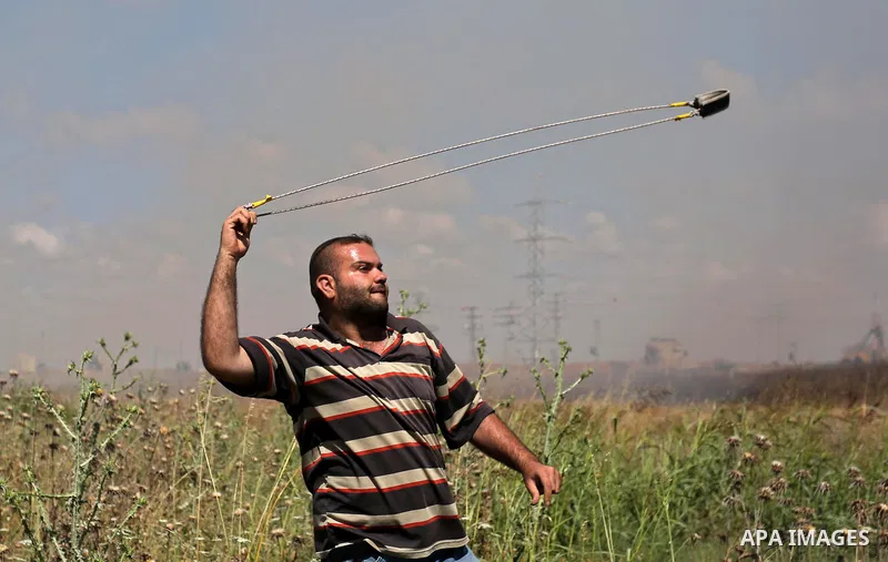 A Palestinian protester uses a slingshot to hurl stones towards Israeli security forces during clashes following a protest against the blockade on Gaza Strip, near Nahal Oz crossing east of Gaza City on May 19, 2017. Pho...