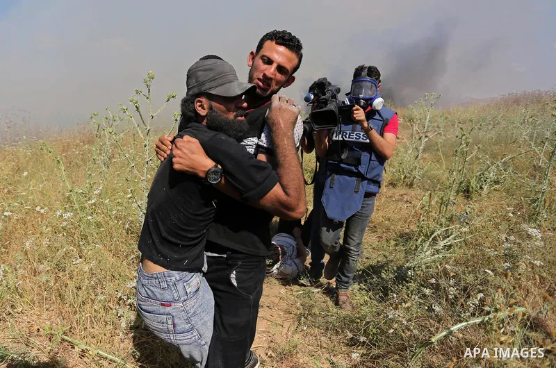 A Palestinian protester carries a handicapped comrade during clashes with Israeli security forces following a protest against the blockade on Gaza Strip, near Nahal Oz crossing east of Gaza City on May 19, 2017. Photo by...