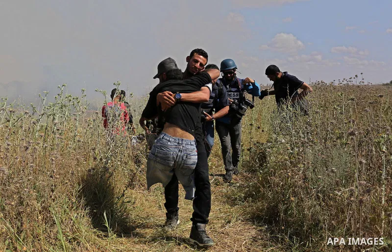 A Palestinian protester carries a handicapped comrade during clashes with Israeli security forces following a protest against the blockade on Gaza Strip, near Nahal Oz crossing east of Gaza City on May 19, 2017. Photo by...