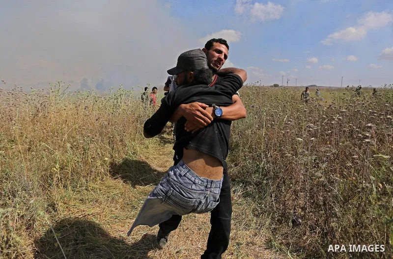 A Palestinian protester carries a handicapped comrade during clashes with Israeli security forces following a protest against the blockade on Gaza Strip, near Nahal Oz crossing east of Gaza City on May 19, 2017. Photo by...