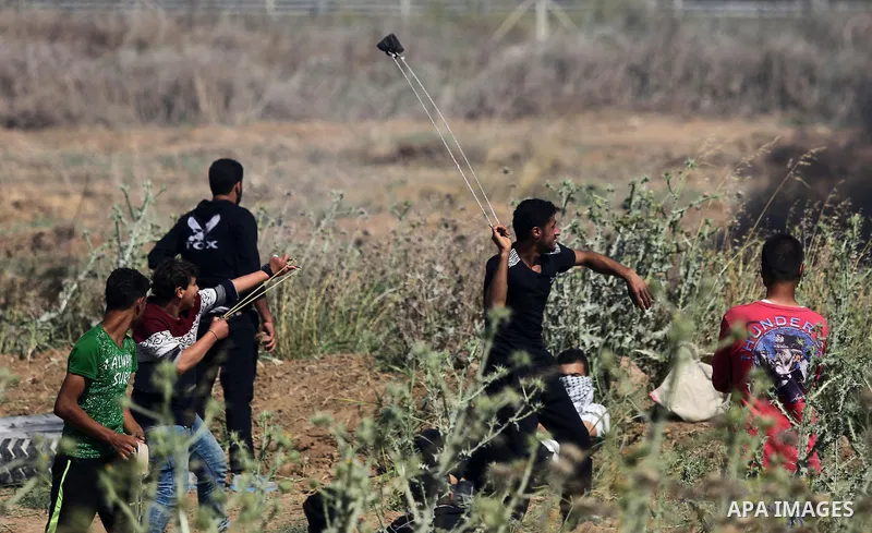 Palestinian protesters use a slingshot to hurl stones towards Israeli security forces during clashes following a protest against the blockade on Gaza Strip, near Nahal Oz crossing east of Gaza City on May 19, 2017. Photo...