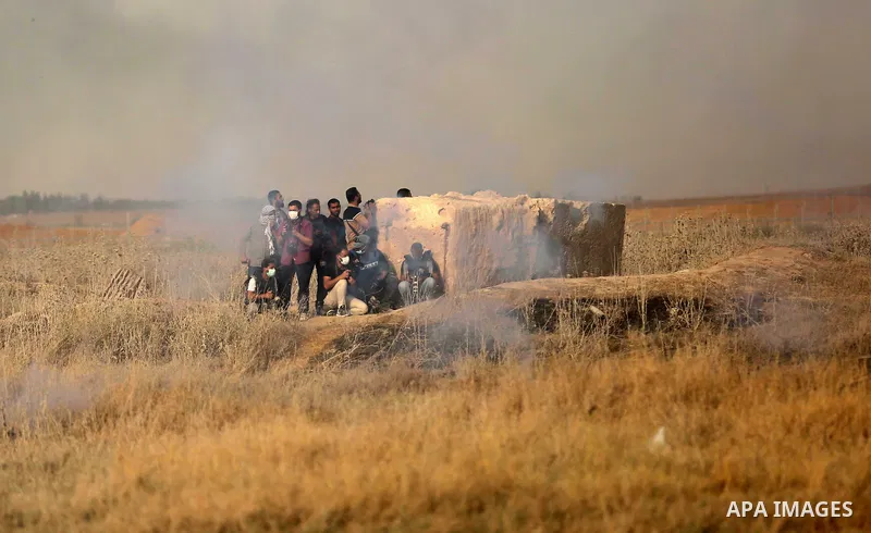 Palestinian photographers take cover from tear gas canister fired by Israeli security forces during clashes following a protest against the blockade on Gaza Strip, near the border fence east of Gaza City on May 22, 2017....