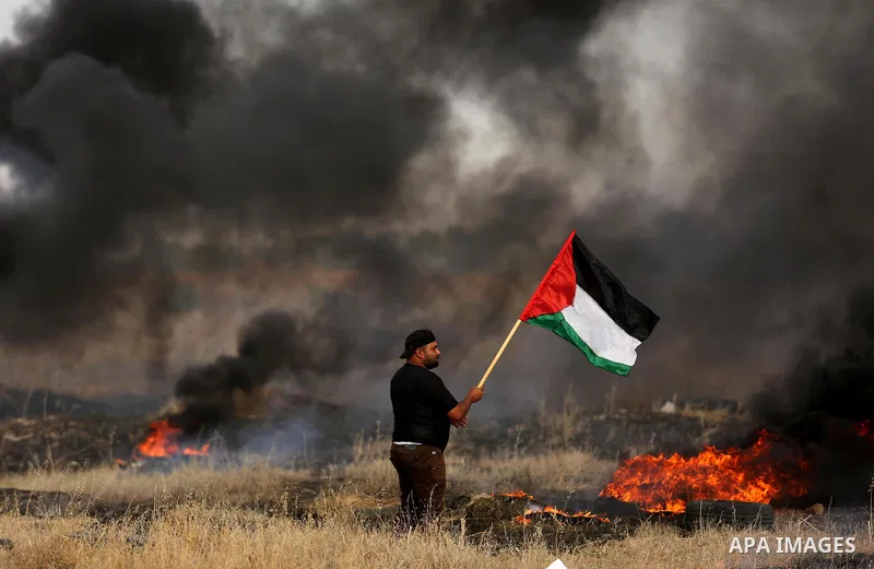 A Palestinian protester waves the national flag during clashes with Israeli security forces following a protest against the blockade on Gaza Strip, near the border fence east of Gaza City on May 22, 2017. Photo by Ashraf...