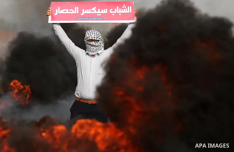 A Palestinian protester holds placards near burning tires during clashes with Israeli security forces following a protest against the blockade on Gaza Strip, near the border fence east of Gaza City on May 22, 2017. Photo...