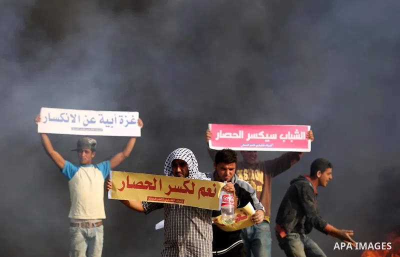 Palestinian protesters hold placards near burning tires during clashes with Israeli security forces following a protest against the blockade on Gaza Strip, near the border fence east of Gaza City on May 22, 2017. Photo b...