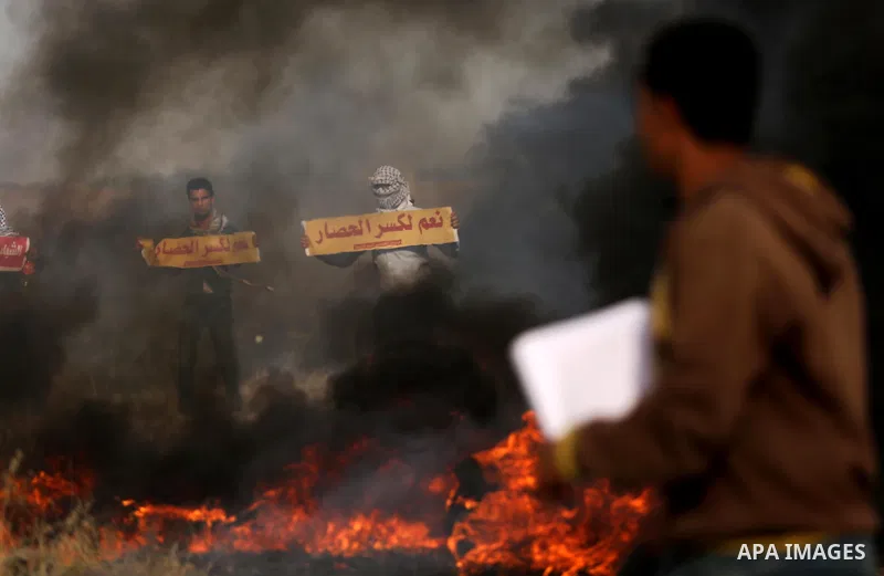 Palestinian protesters hold placards near burning tires during clashes with Israeli security forces following a protest against the blockade on Gaza Strip, near the border fence east of Gaza City on May 22, 2017. Photo b...