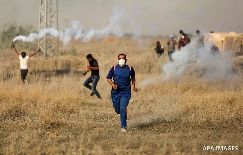Palestinian protesters run for cover from tear gas canister fired by Israeli security forces during clashes following a protest against the blockade on Gaza Strip, near the border fence east of Gaza City on May 22, 2017....
