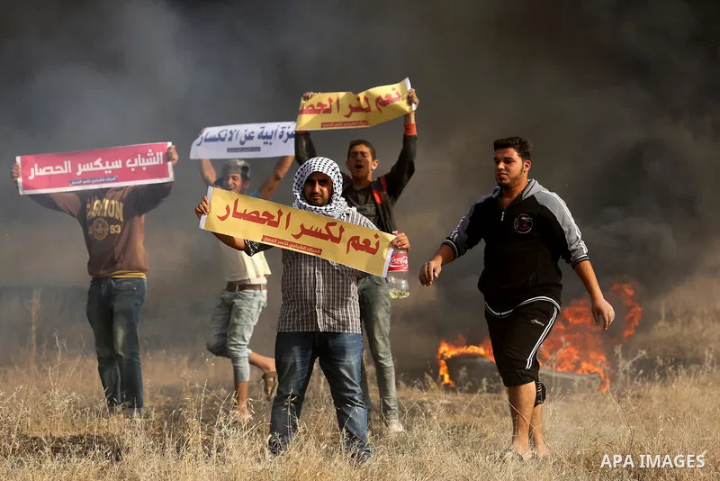 Palestinian protesters hold placards near burning tires during clashes with Israeli security forces following a protest against the blockade on Gaza Strip, near the border fence east of Gaza City on May 22, 2017. Photo b...