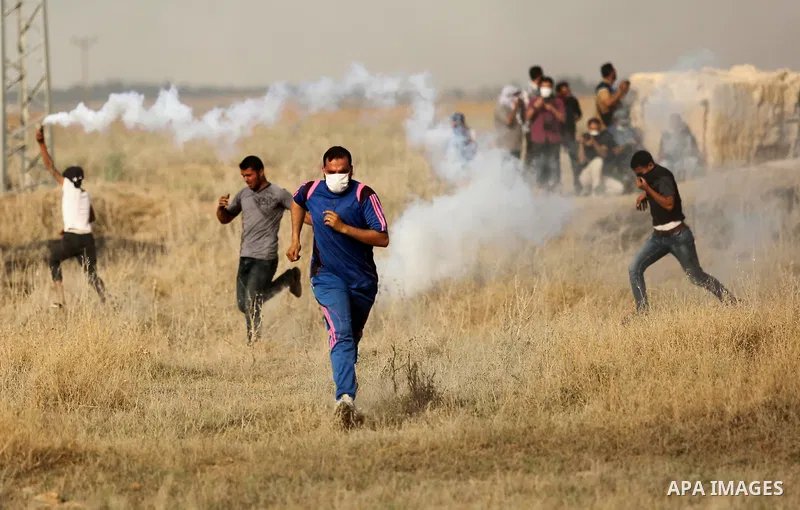 Palestinian protesters run for cover from tear gas canister fired by Israeli security forces during clashes following a protest against the blockade on Gaza Strip, near the border fence east of Gaza City on May 22, 2017....