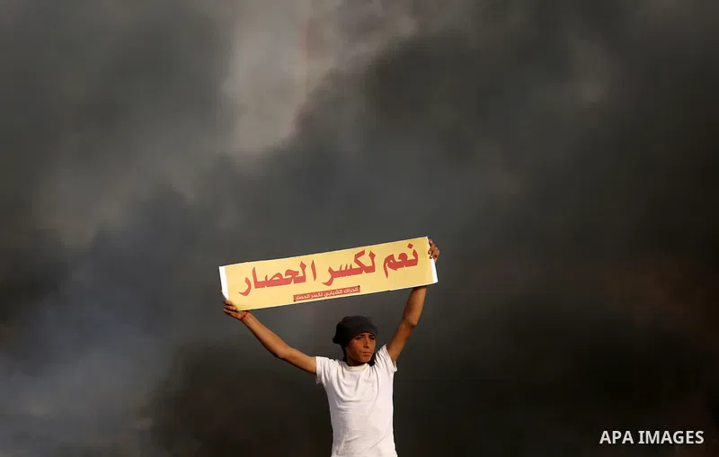 A Palestinian protester holds placards near burning tires during clashes with Israeli security forces following a protest against the blockade on Gaza Strip, near the border fence east of Gaza City on May 22, 2017. Photo...