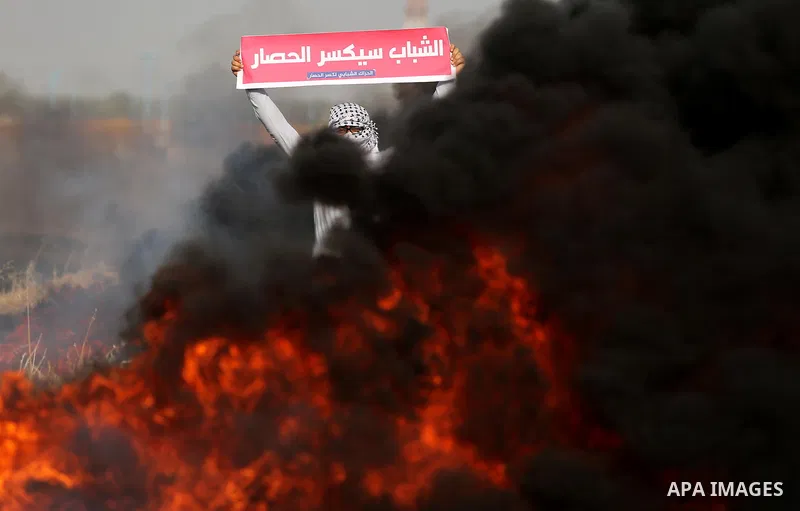 A Palestinian protester holds placards near burning tires during clashes with Israeli security forces following a protest against the blockade on Gaza Strip, near the border fence east of Gaza City on May 22, 2017. Photo...