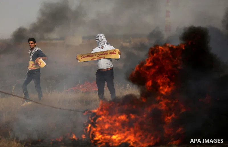Palestinian protesters hold placards near burning tires during clashes with Israeli security forces following a protest against the blockade on Gaza Strip, near the border fence east of Gaza City on May 22, 2017. Photo b...
