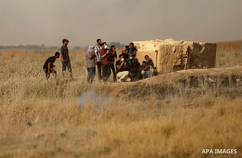 Palestinian photographers take cover from tear gas canister fired by Israeli security forces during clashes following a protest against the blockade on Gaza Strip, near the border fence east of Gaza City on May 22, 2017....