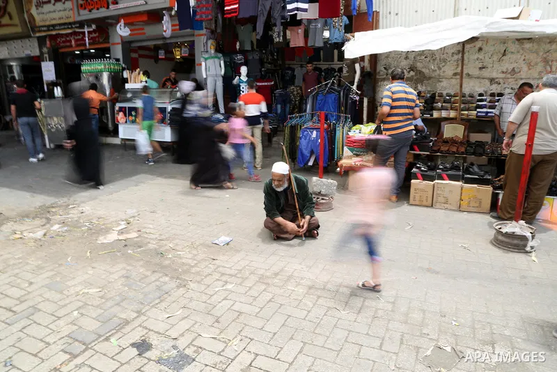 A Palestinian elderly beggar man asks for money as other Palestinians shop at a market ahead of the Muslim holy month of Ramadan, in Gaza city, on May 25, 2017 as the faithful prepare to start fasting. Photo by Ashraf Am...