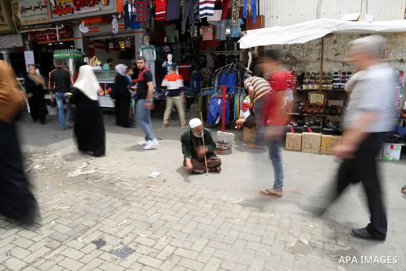 A Palestinian elderly beggar man asks for money as other Palestinians shop at a market ahead of the Muslim holy month of Ramadan, in Gaza city, on May 25, 2017 as the faithful prepare to start fasting. Photo by Ashraf Am...