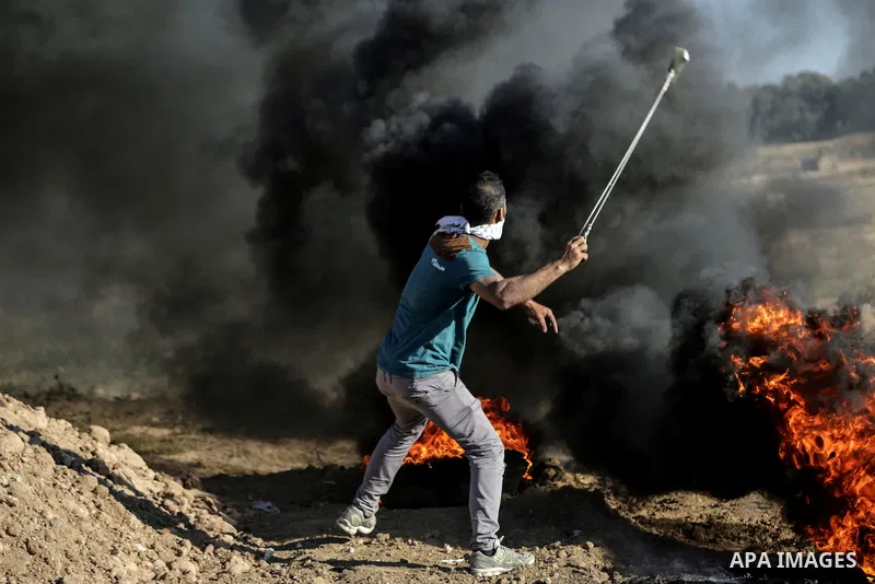 A Palestinian protester uses a slingshot to hurl stones towards Israeli security forces during clashes near the border between Israel and Central Gaza Strip May 26, 2017. Photo by Nidal Alwaheidi
