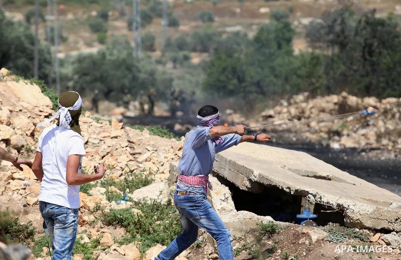 A Palestinian protester uses a slingshot to hurl stones towards Israeli security forces during clashes following a demonstration against the expropriation of Palestinian land by Israel in the village of Kfar Qaddum, near...