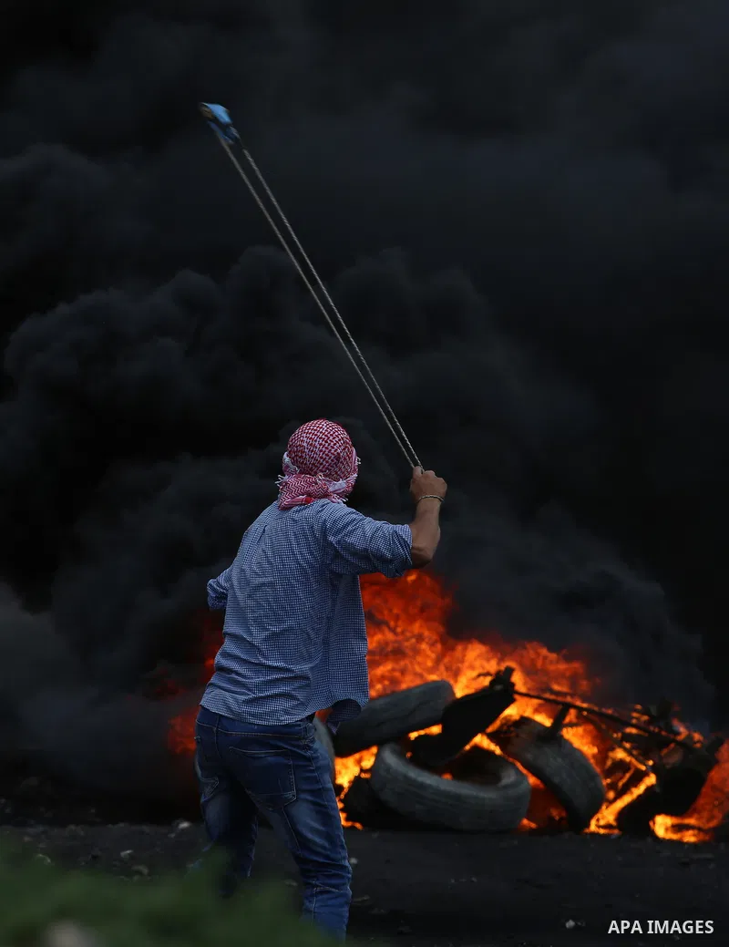 A Palestinian protester uses a slingshot to hurl stones towards Israeli security forces during clashes following a demonstration against the expropriation of Palestinian land by Israel in the village of Kfar Qaddum, near...