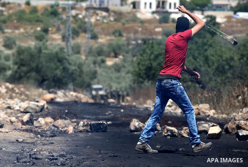 A Palestinian protester uses a slingshot to hurl stones towards Israeli security forces during clashes following a demonstration against the expropriation of Palestinian land by Israel in the village of Kfar Qaddum, near...