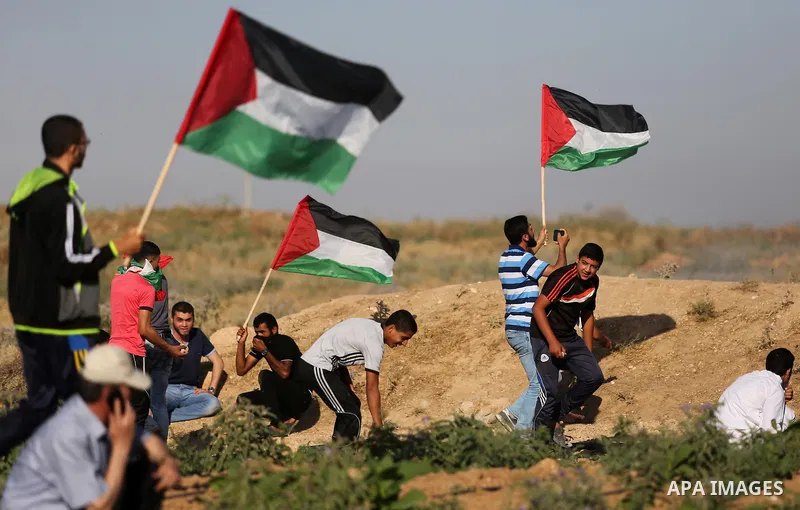 Palestinian protesters wave their national flag as they watch fellow demonstrators clashing with Israeli security forces following a protest near the border fence east of Jabalia refugee camp, against the blockade on the...
