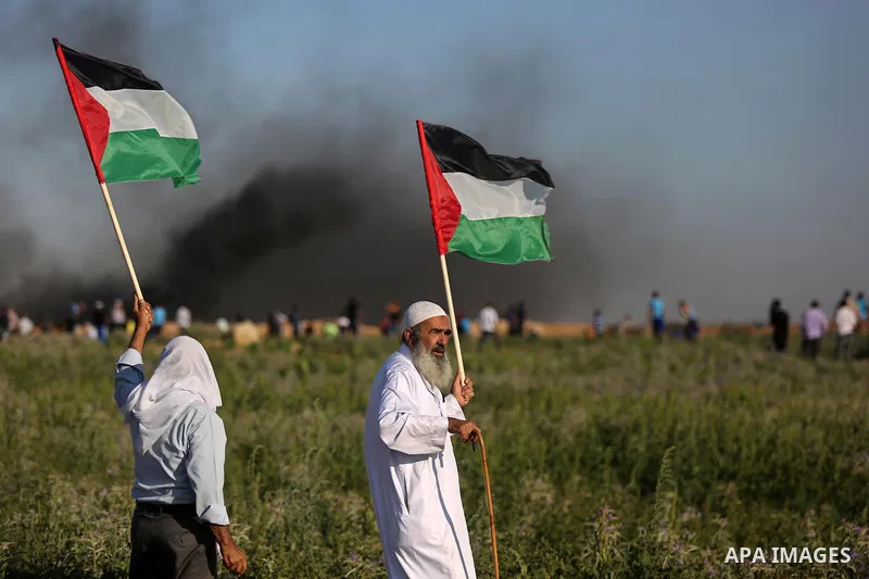Palestinian protesters wave their national flag as they watch fellow demonstrators clashing with Israeli security forces following a protest near the border fence east of Jabalia refugee camp, against the blockade on the...