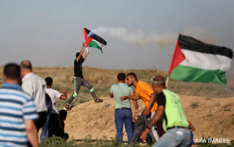A Palestinian protester hold the national flag and a tear gas canister fired by Israeli security froces during clashes following a demonstration against the blockade on the Gaza Strip, near the border fence east of Jabal...
