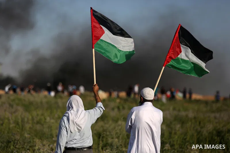 Palestinian protesters wave their national flag as they watch fellow demonstrators clashing with Israeli security forces following a protest near the border fence east of Jabalia refugee camp, against the blockade on the...